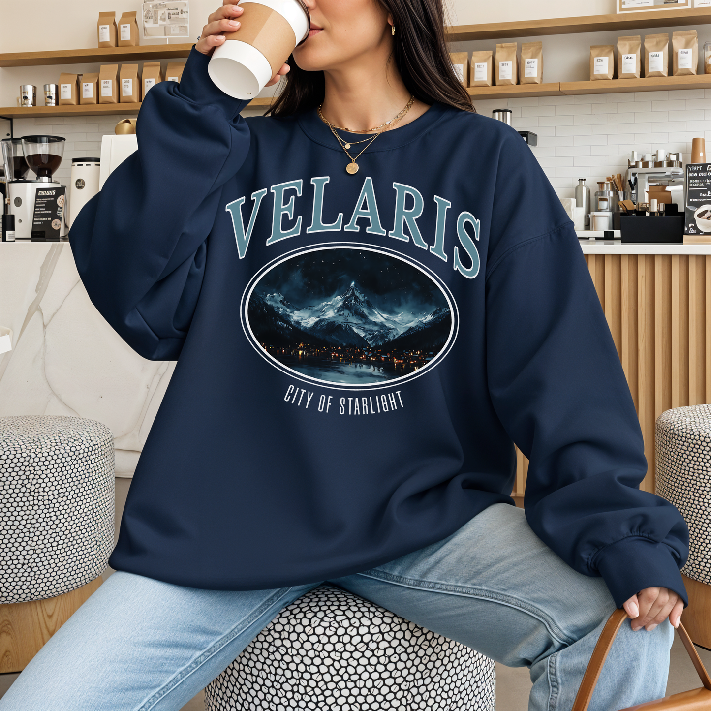 Person wearing a navy blue sweatshirt with 'VELARIS City of Starlight' design, sitting in a cafe.