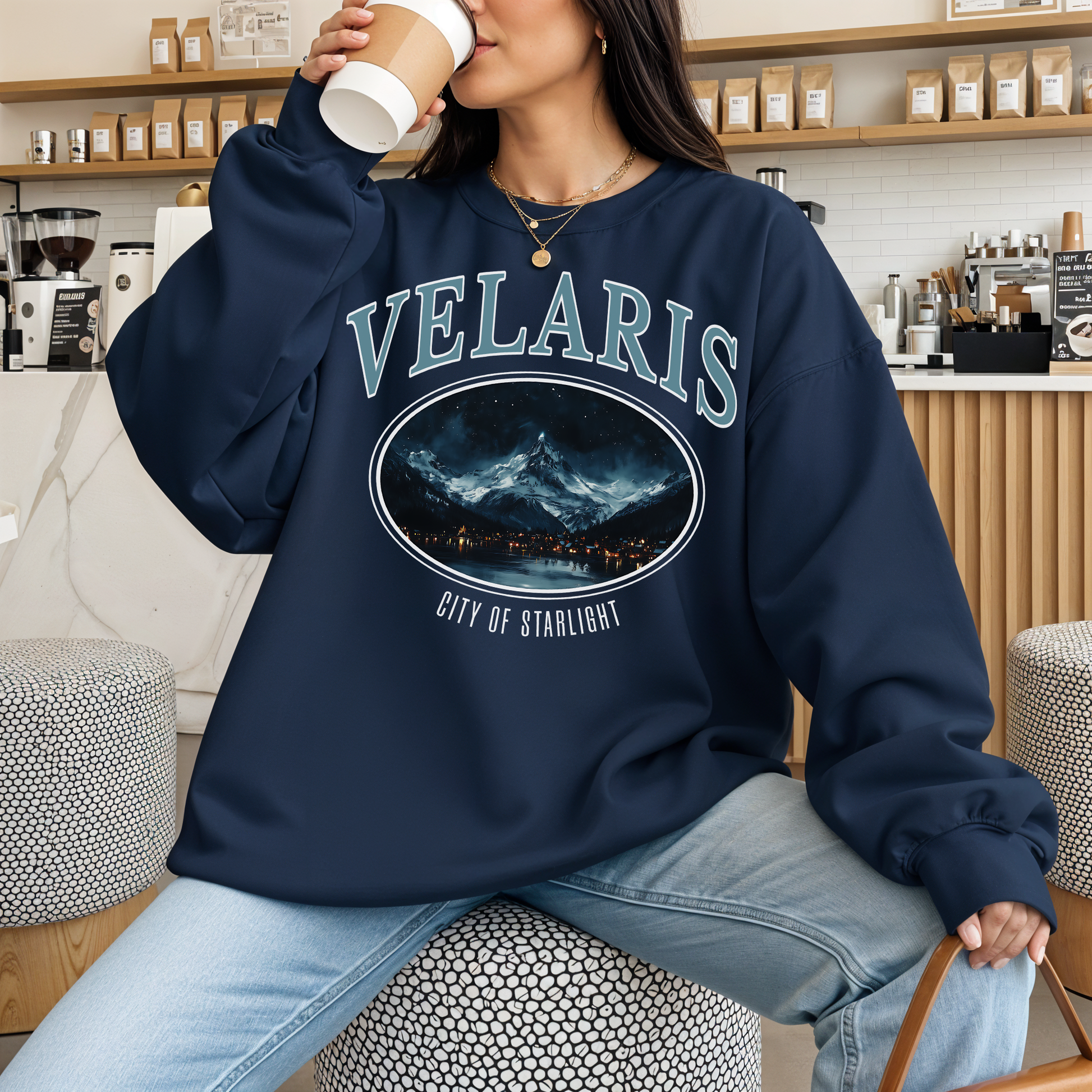 Person wearing a navy blue sweatshirt with 'VELARIS City of Starlight' design, sitting in a cafe.
